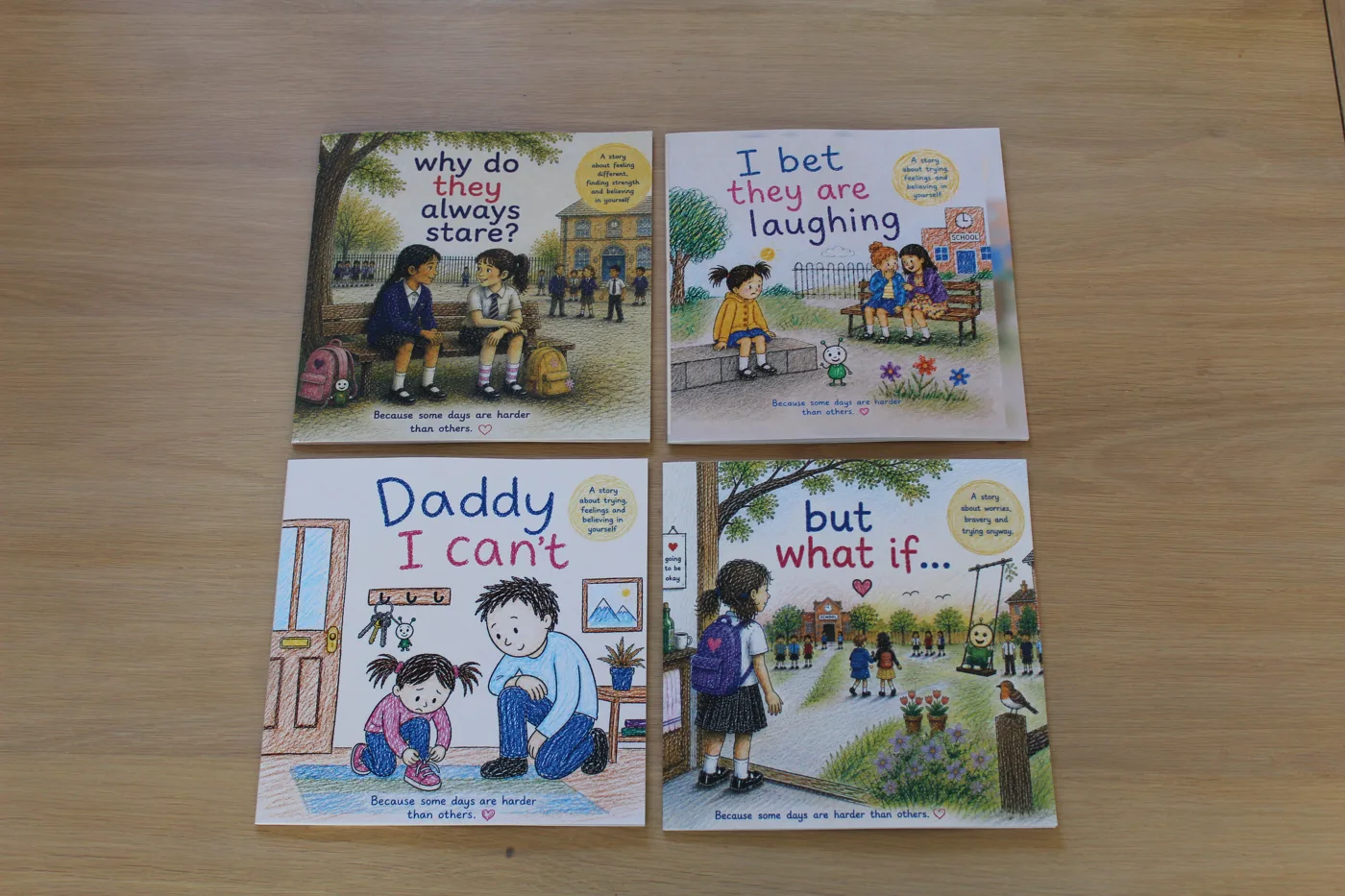 Four picture books laid out on a wooden table: Why Do They Always Stare?, I Bet They Are Laughing, Daddy I Can't and But What If...